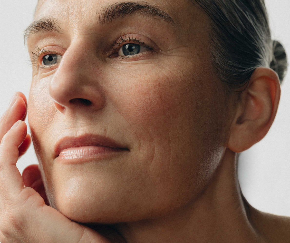 Nahaufnahme eines Frauengesichts mit leichten Falten um Augen und Mund, Kinn auf der Hand gestützt